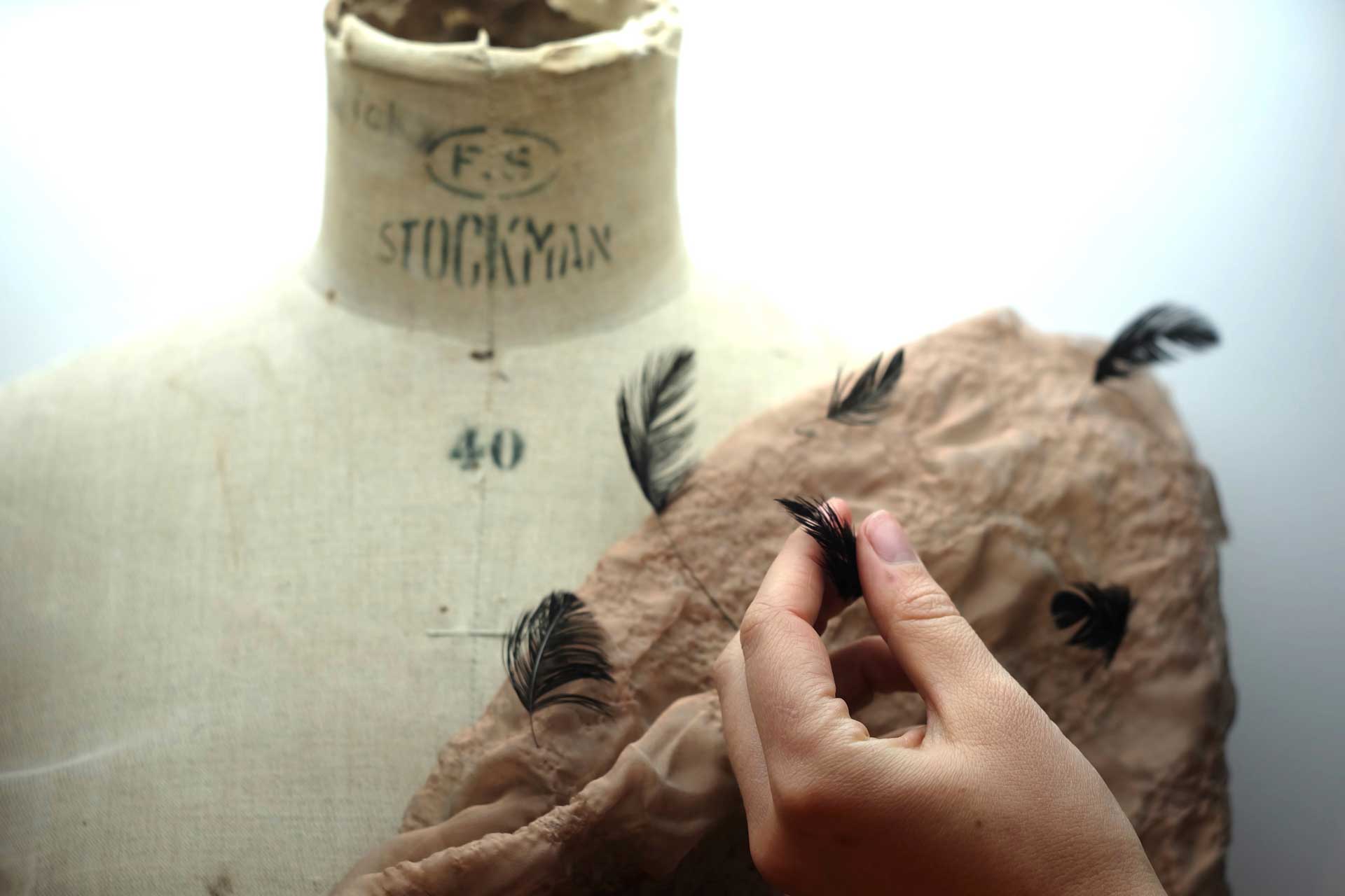 Hand grasping a feather in front of a dress form.