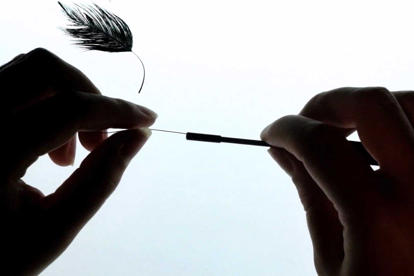 Hands wrapping wire to a feather.